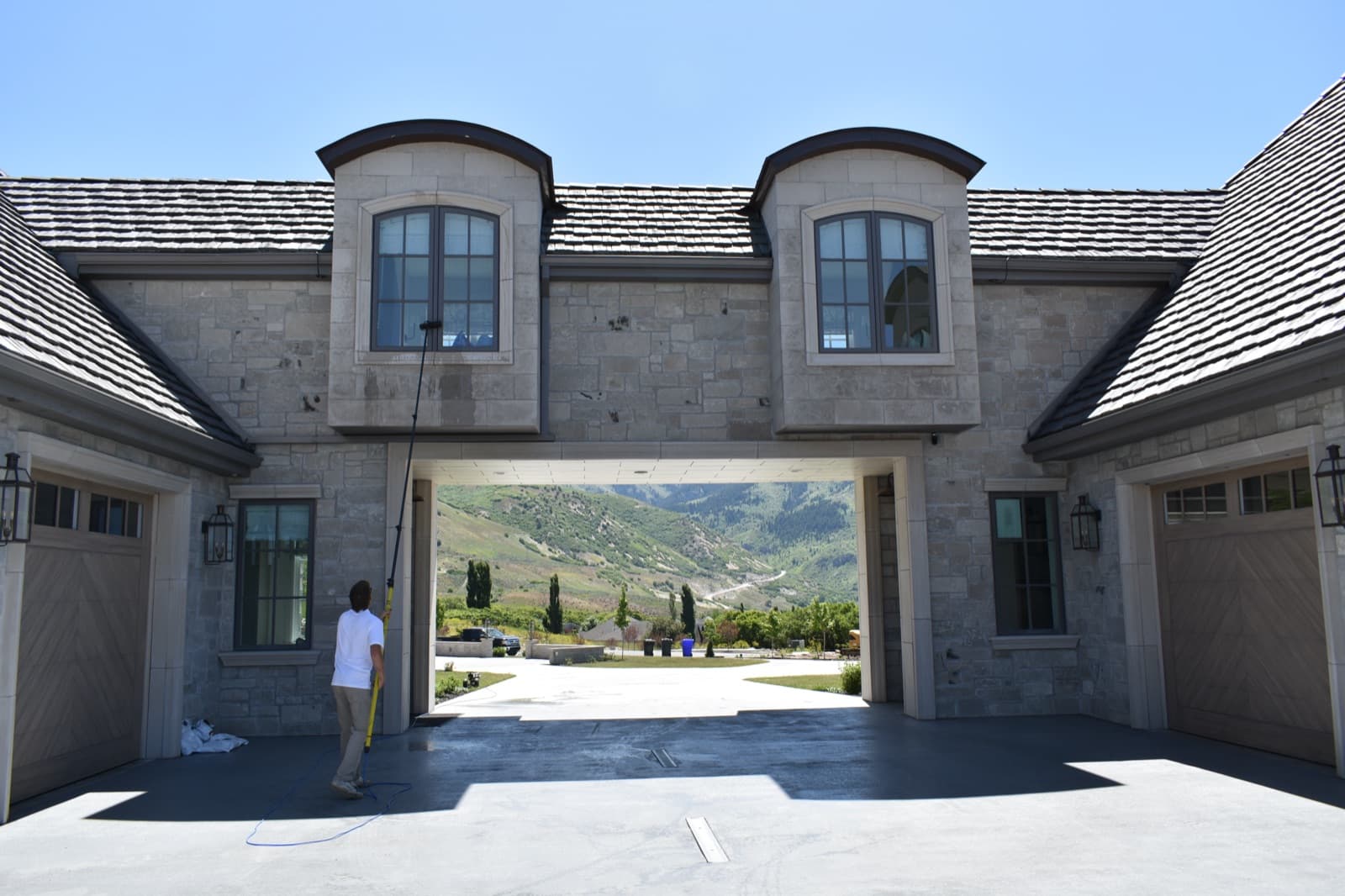 Technician cleaning dormer windows on a stone estate breezeway with mountain valley views