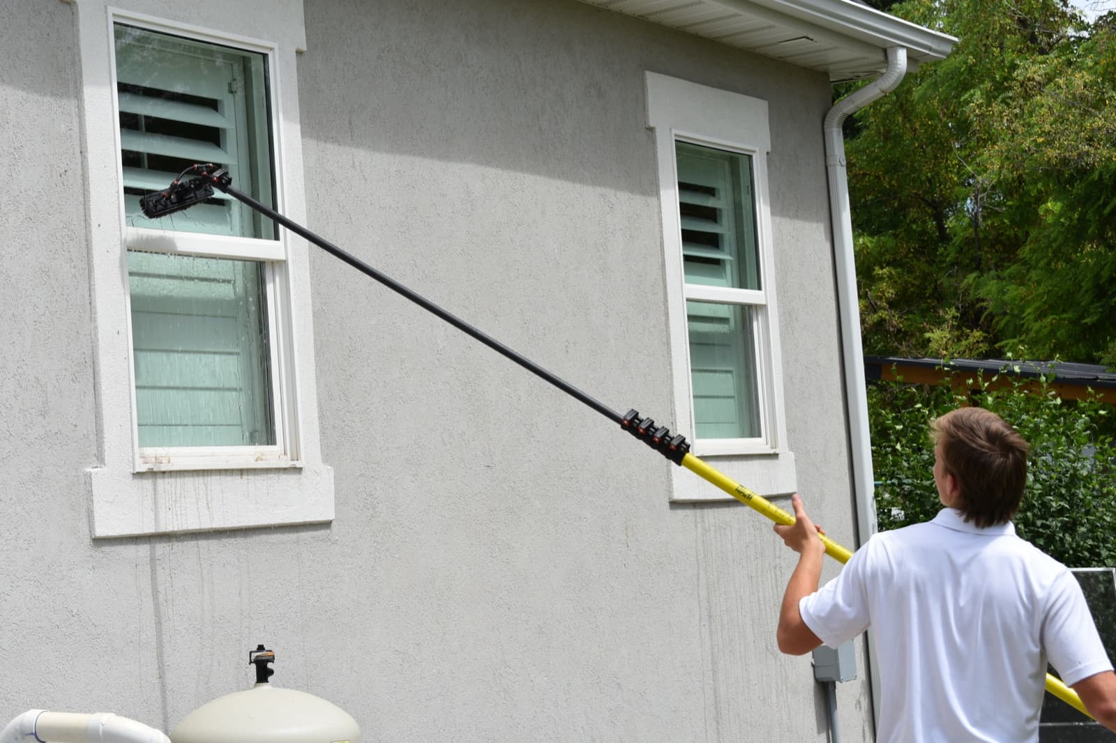 Technician cleaning upper-story windows with a water-fed pole brush at a Utah home